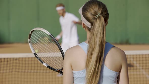 Female hitting tennis ball with racket at sports club, playing with opponent