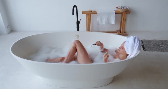 High Angle View of Attractive Woman with Wrapped Head in White Bath Towel Enjoying Foam Bathing