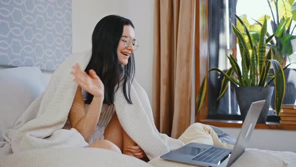 Young Cute Lady Wearing Eyeglasses Waving Hand to Laptop Greeting Friends Via Video Call Sitting in