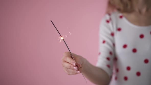 Bengal fire in the hand of a girl on a pink background