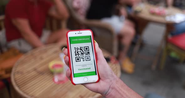 Woman holding mobile phone with coronavirus QR code certification in front of bar