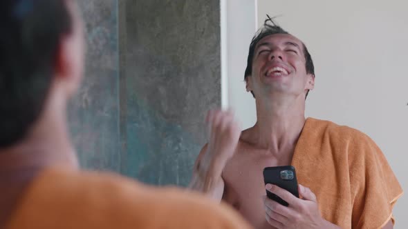 Excited Smiling Man Looking Into Smartphone and Rejoicing at Good News with Towel Standing in the