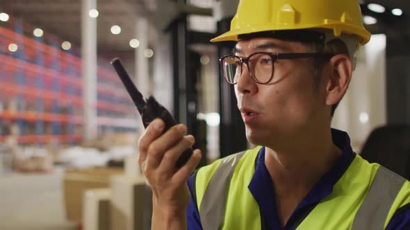 Asian male worker wearing safety suit with helmet talking in warehouse