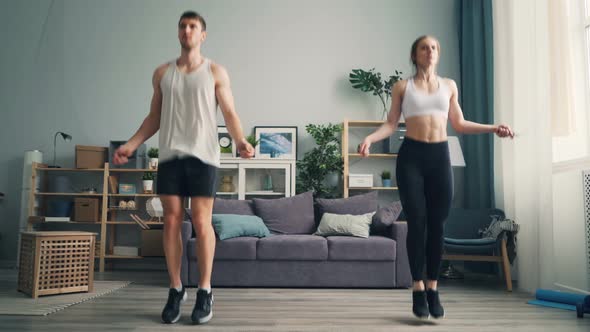 Attractive Girl and Guy Jumping Rope in Studio Apartment Focused on Exercise