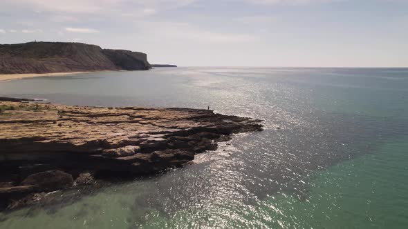 Fly-over alongside rocky Algarve shoreline revealing Praia da Luz - Aerial