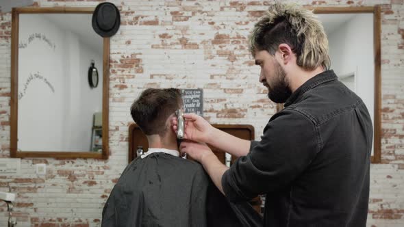 Man Barber Cutting Hair of Male Client with Clipper at Barber Shop