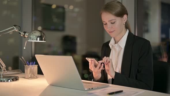 Ambitious Businesswoman Scrolling on Smartphone in Office at Night