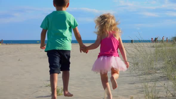 Little Boy and Girl Run Along the Sand To the Sea