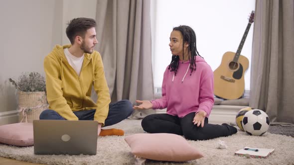 Young African American Girl and Caucasian Boy Sitting on Soft Carpet on the Floor and Chatting