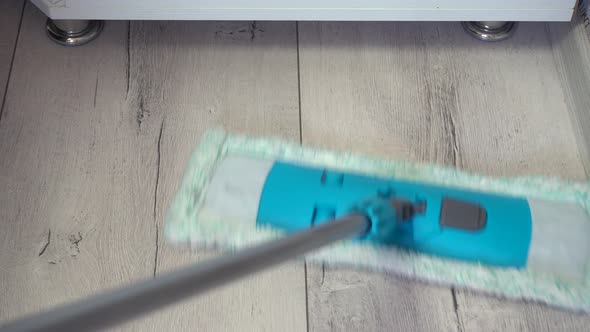 Man Cleaning Floors with Mop on Gray Laminate Surface Near Plinth Wall and Under Cupboard