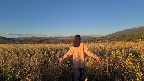 a woman walks through a field with oats