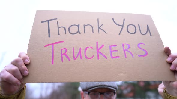 A Poster with the Inscription Thank you Truckers in the Hands of an Elderly Man in Winter Clothes