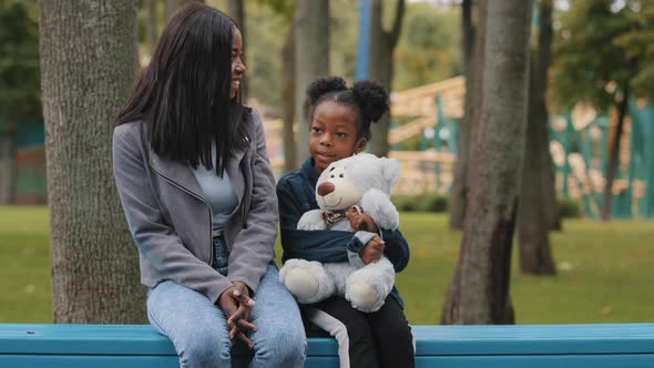 Mom and Daughter Sitting on Bench Child Holding Teddy Bear Little Girl Showing Five Fingers African