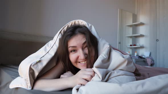 Pretty Girl Hides in Blanket on Large Bed in Hotel Room