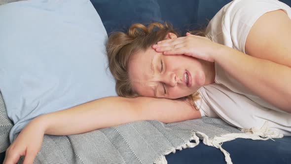 Young Woman Lies on the Bed with Her Eyes Closed and Massages the Temples of Head Due to Migraines