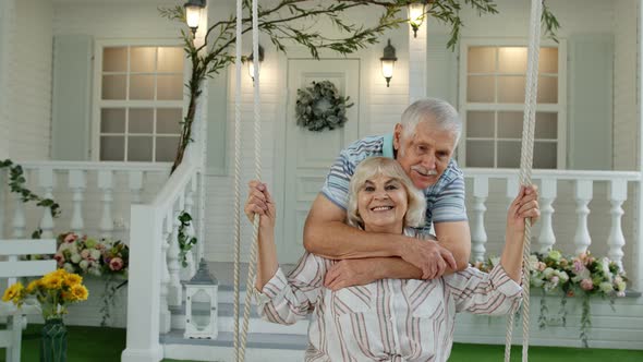 Senior Couple Together in Front Yard at Home. Man Swinging Woman During Coronavirus Quarantine