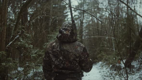 Back view of a hunter walking in the snow with a rifle and camouflage during hunting trip, winter hu