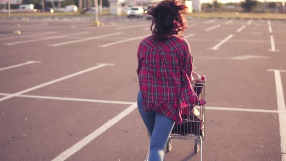 Back View of a Young Woman Sitting in the Grocery Cart While Her Friend is Pushing Her Behind in the