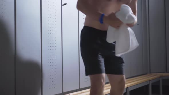 Young Handsome Caucasian Sportsman with Naked Torso Entering Dressing Room, Sitting Down and Rubbing