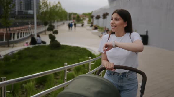 The Girl Walks with a Stroller in the Park and Talks on a Smart Watch