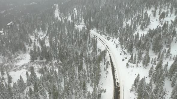 Aerial tilt shot revealing a dangerous mountain road covered by snow on a foggy day