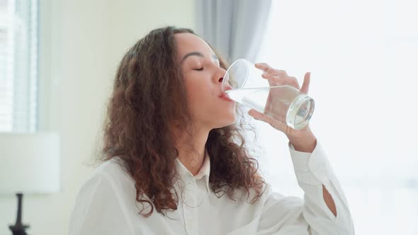 Close up of Latino woman sit on bed, hold a glass of water in bedroom.