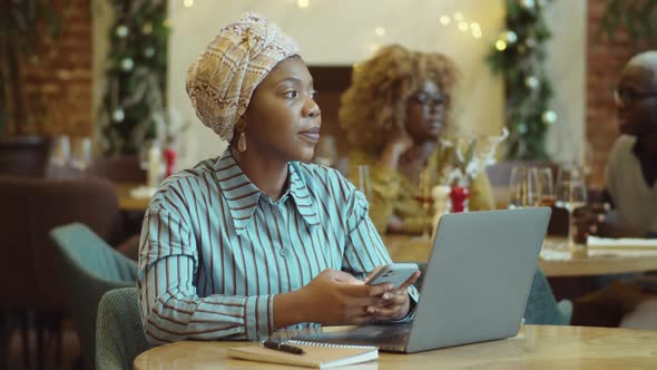 Black Woman Using Phone and Laptop in Cafe