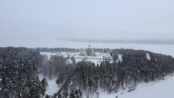 Snow-covered Pazaislis Monastery during snowfall, aerial flying towards view