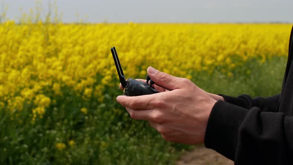 Close-up shot of drone remote control in men's hands. A man flying on a drone over a yellow field