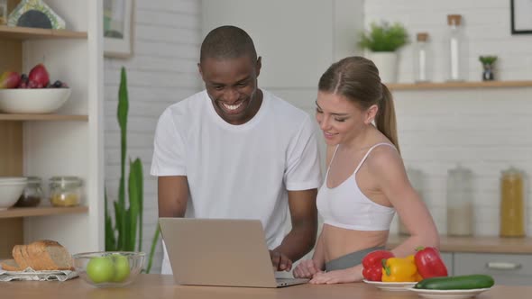 Athletic Woman and African Man Working on Laptop in Kitchen