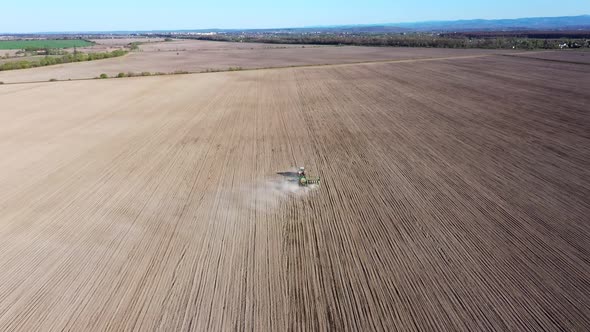 Aerial view of tractor with harrow system plowing ground on cultivated farm field