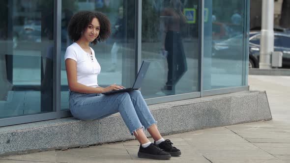 Pleasant Young Positive Curly Hair African American Ethnic Woman Enjoying Work at Laptop Smiling