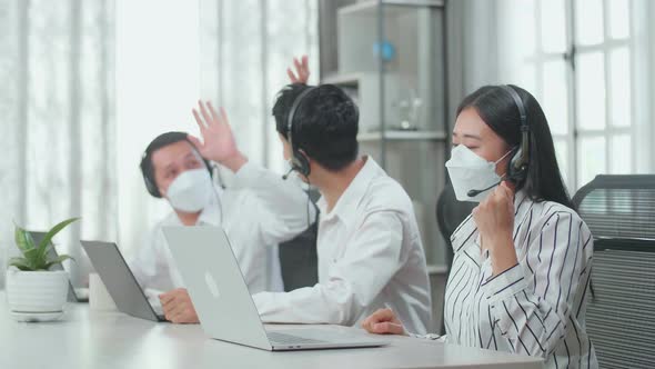 Three Asian Call Centre Agents Wearing Headsets, Masks And Being Happy Due To Success Working