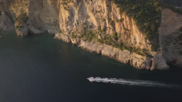 Aerial view of motor boat sailing along the high cliffs at sunset, Montenegro.