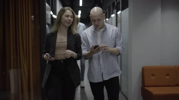 Positive Young Caucasian Coworkers Walking Along Office Corridor Talking