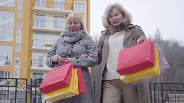 Senior Caucasian Women Strolling on City Street After Shopping. Happy Active Middle-aged Retirees