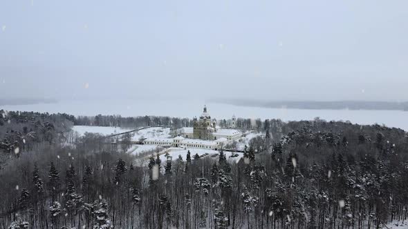 Pazailis monastery in Lithuania covered in snow during snowfall, aerial ascend view