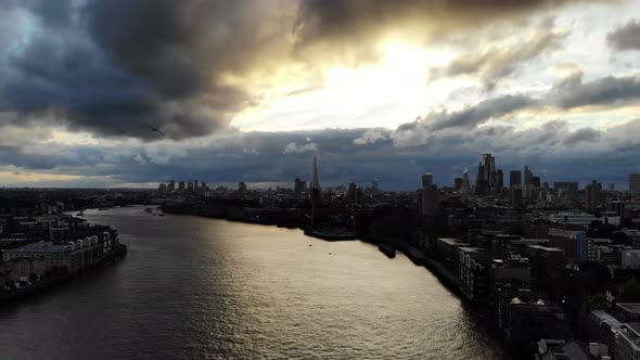 Reverse aerial view of London skyline under dramatic stormy dark clouds flying over river Thames