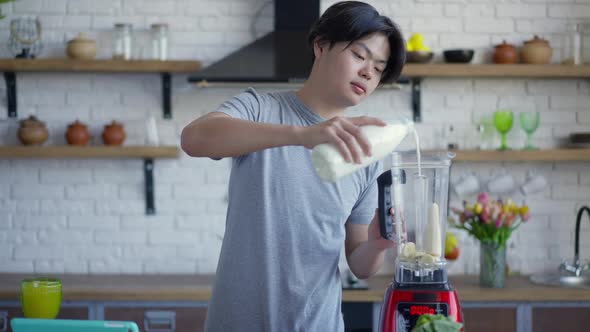 Middle Shot Portrait of Young Man Pouring Milk in Blender with Chopped Banana