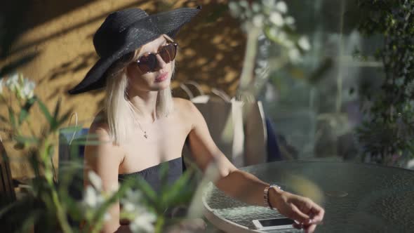 Beautiful Stylish Young Blonde Woman Smoking Cigarettes Outdoors in Han and Sunglasses