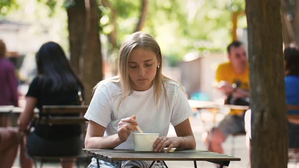 Young Female is Having a Rest While Eating Ice Cream Sitting at Table on a Summer Terrace of Cafe