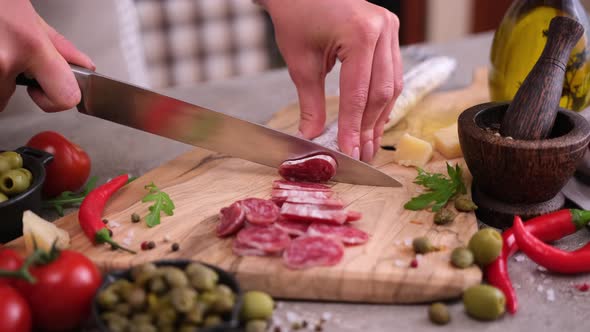 Woman Slicing Fuet Sausage with Knife at Domestic Kitchen