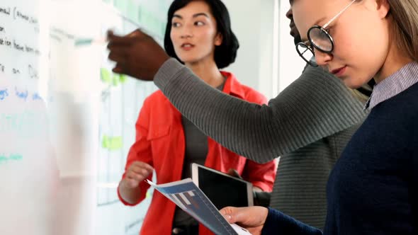 Female executive looking at document while colleagues discussing over whiteboard 4k