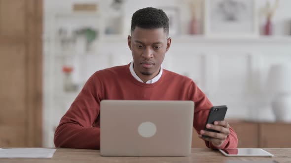 African Man using Smartphone while using Laptop in Office