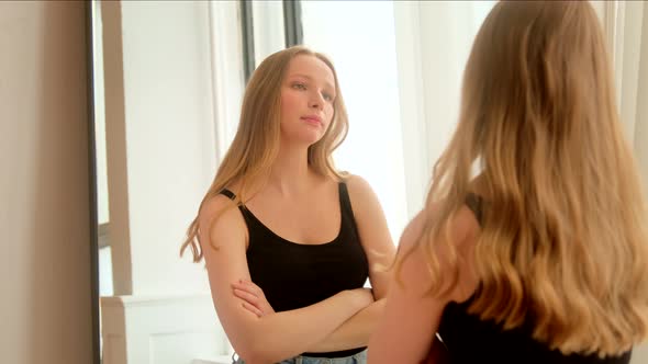 Displeased woman looking at reflection in the mirror unsatisfied and worried about appearance.