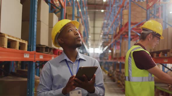 African american male worker with helmet using tablet in warehouse