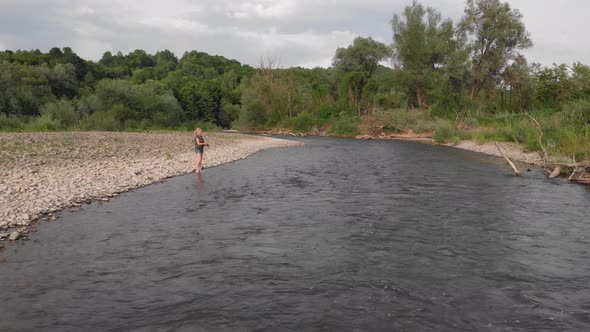 Beautiful young woman in a green vest fishing with a spinning rod on a mountain river