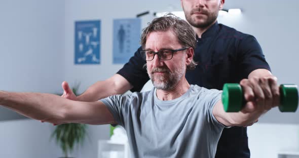Crop Therapist Helping Mature Man to Exercise with Dumbbells