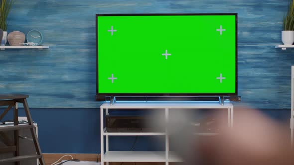 Selective Focus of Hand Holding Remote Control and Switching Channels on Green Screen Tv