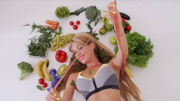 Young Woman Lies Among Fresh Vegetables Holding Measuring Tape